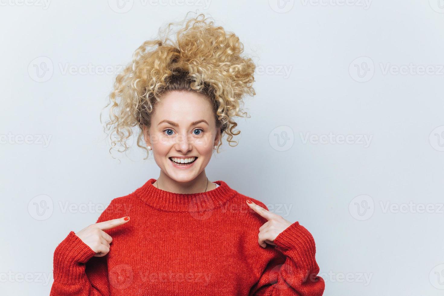 bedårande glad kvinna med glada uttryck, bär lös röd tröja, indikerar på tomt kopia utrymme, annonserar ny outfit, isolerad över vit bakgrund. människor, kläder och reklam foto