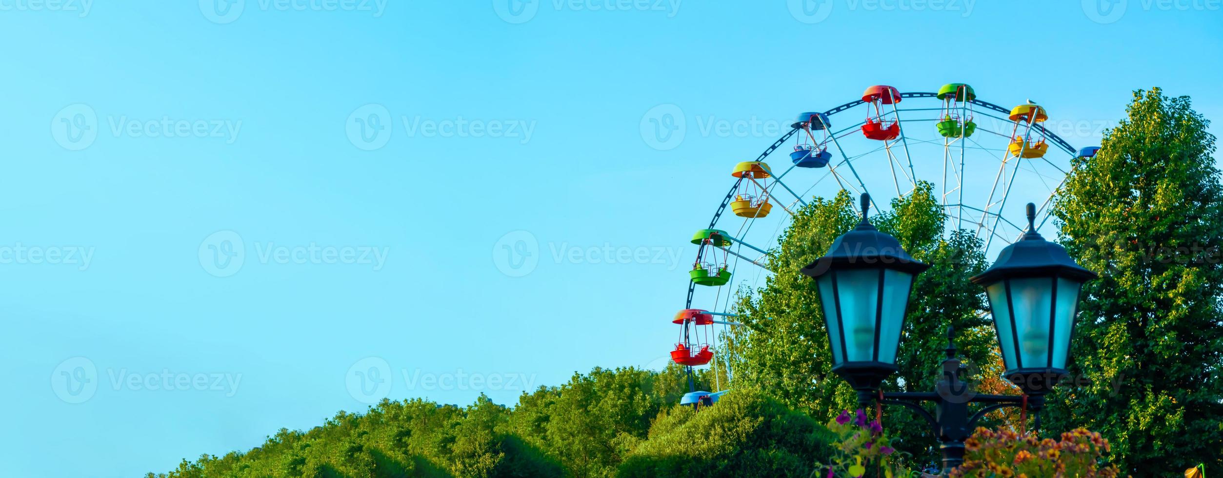 landskap av en nöjespark med lykta dekorerad med blommor bakgrund toppen av ett pariserhjul visar ovanför trädtopparna mot en blå himmel. foto