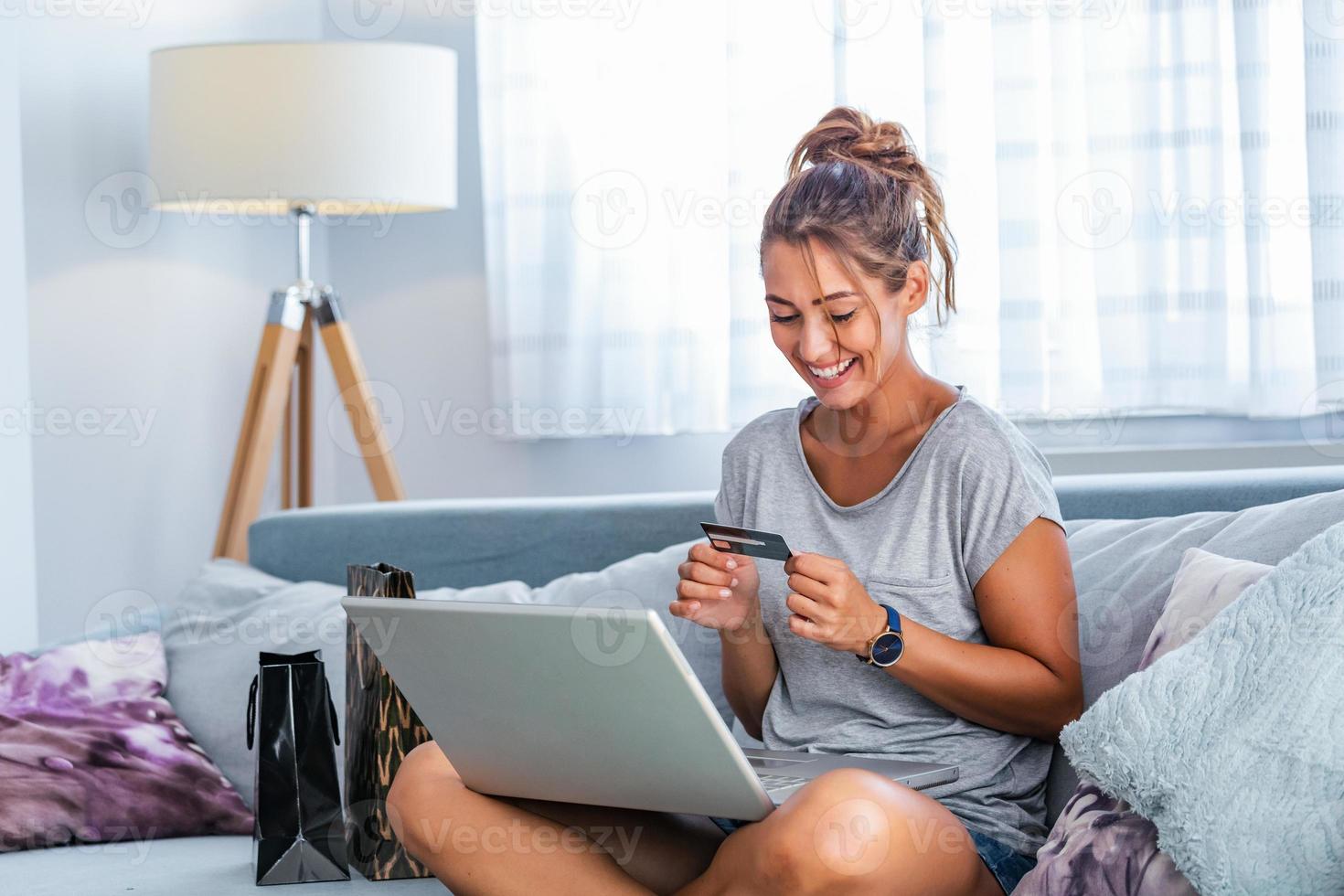 ung kvinna innehav kreditera kort och använder sig av bärbar dator dator. uppkopplad handla begrepp. Lycklig kvinna håller på med uppkopplad handla på Hem foto