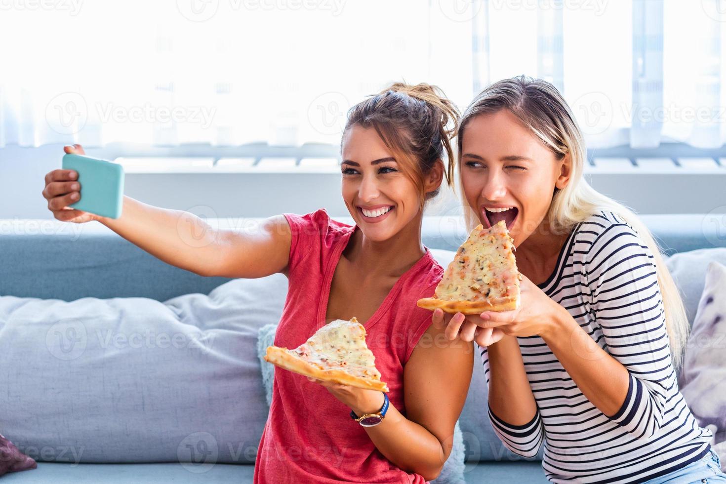 vänner äter pizza och leende för selfie. de är delning pizza och framställning selfie Foto på mobil smart telefon. de är har fest på Hem, äter pizza och har roligt.