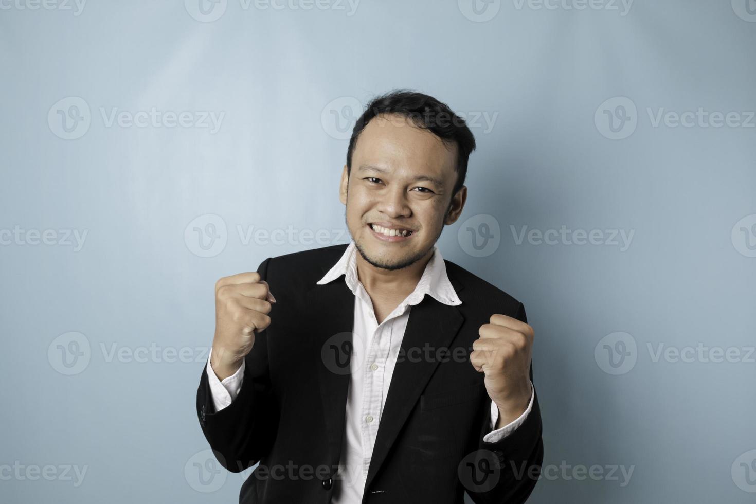 en ung asiatisk man med en Lycklig framgångsrik uttryck bär kostym isolerat förbi blå bakgrund foto