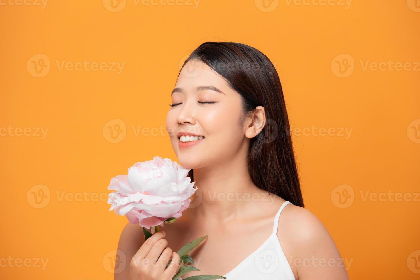 ung kvinna sniffa rosa pion blomma stängd henne ögon på gul bakgrund foto