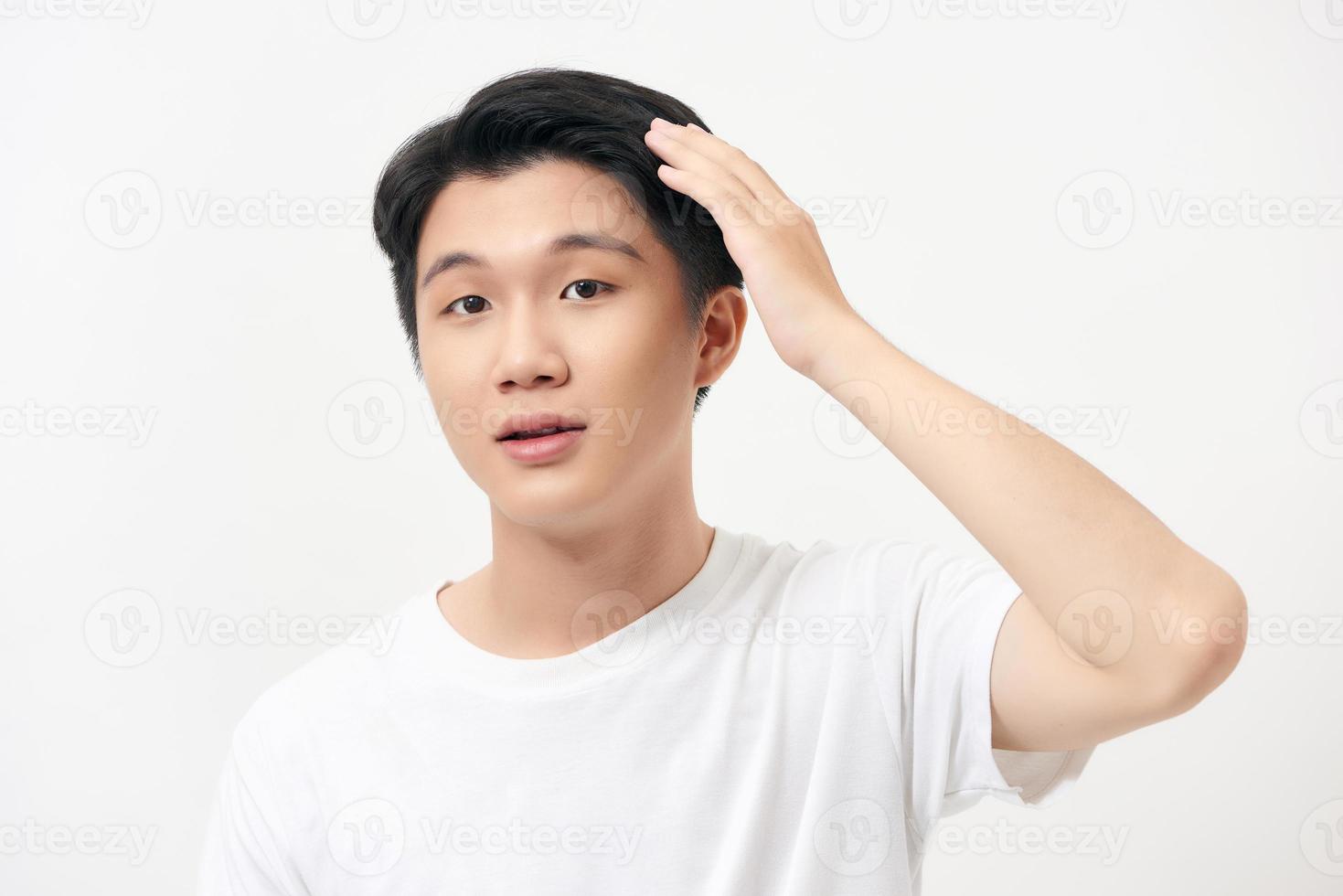 porträtt av en ung man innehav ett hand Bakom hans huvud, leende, på en vit bakgrund foto