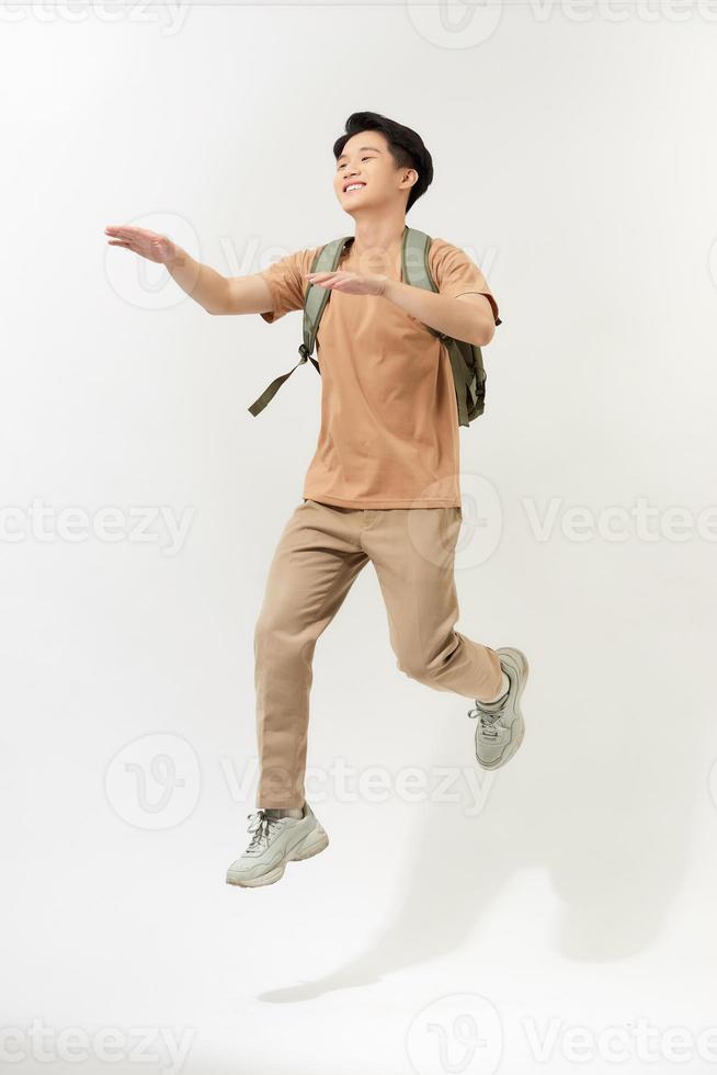 Lycklig leende ung man med ryggsäck Hoppar i luft över vit bakgrund foto