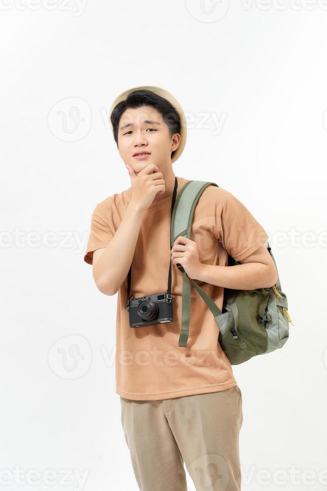 ung turist i hatt med kamera och ryggsäck tänkande över vit bakgrund. besluta var till flyga för semester. studio skott foto
