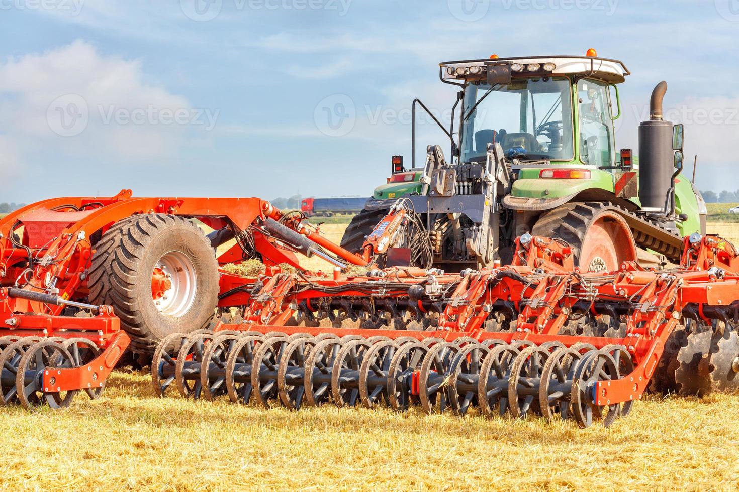 en kraftfull jordbruks traktor kombinerad med en röd flera rader skiva harv på en sommar dag. foto