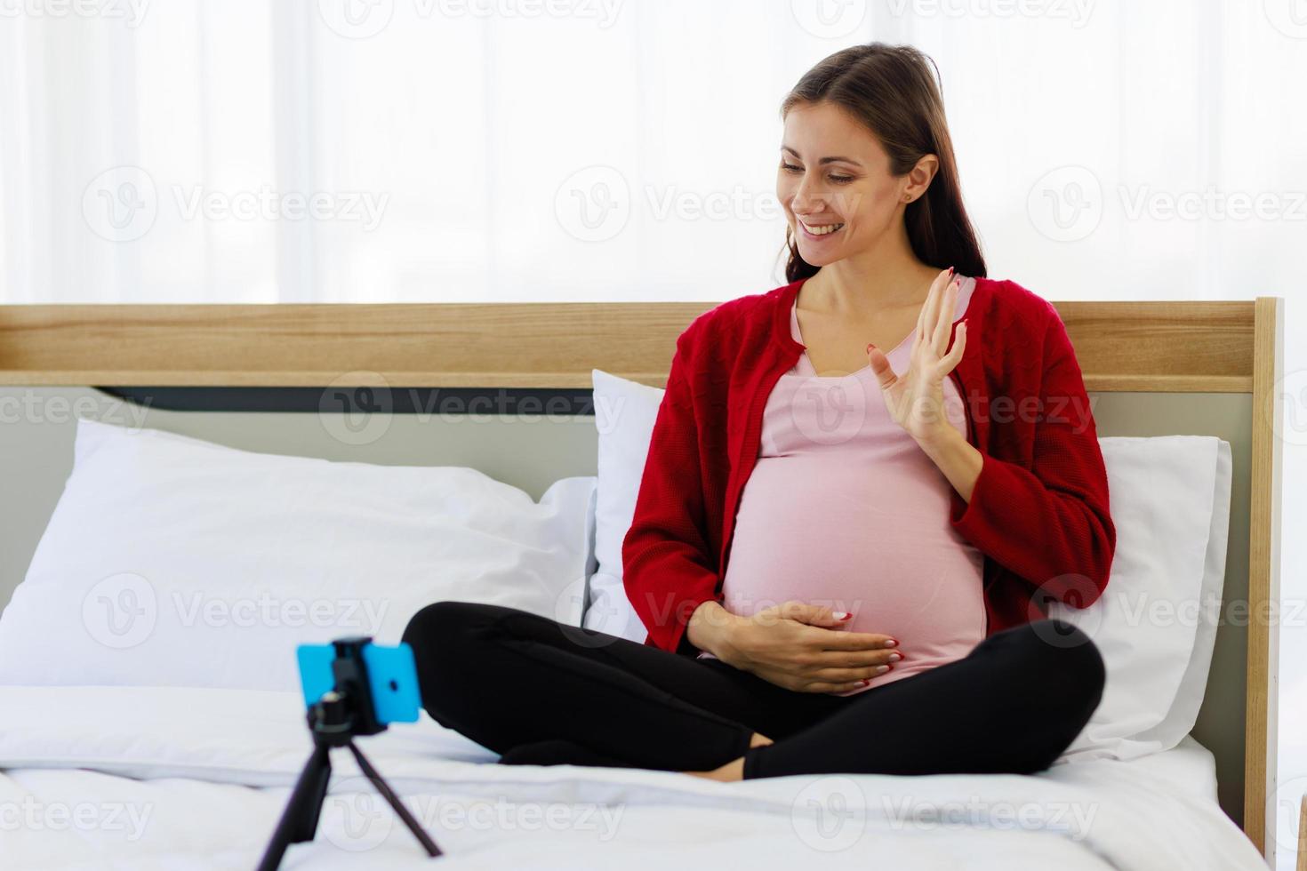 skön caucasian kvinna lyckligt gravid på en video ring upp på henne smartphone. ny moms kommunicera trådlöst med modern kommunikation enheter. foto