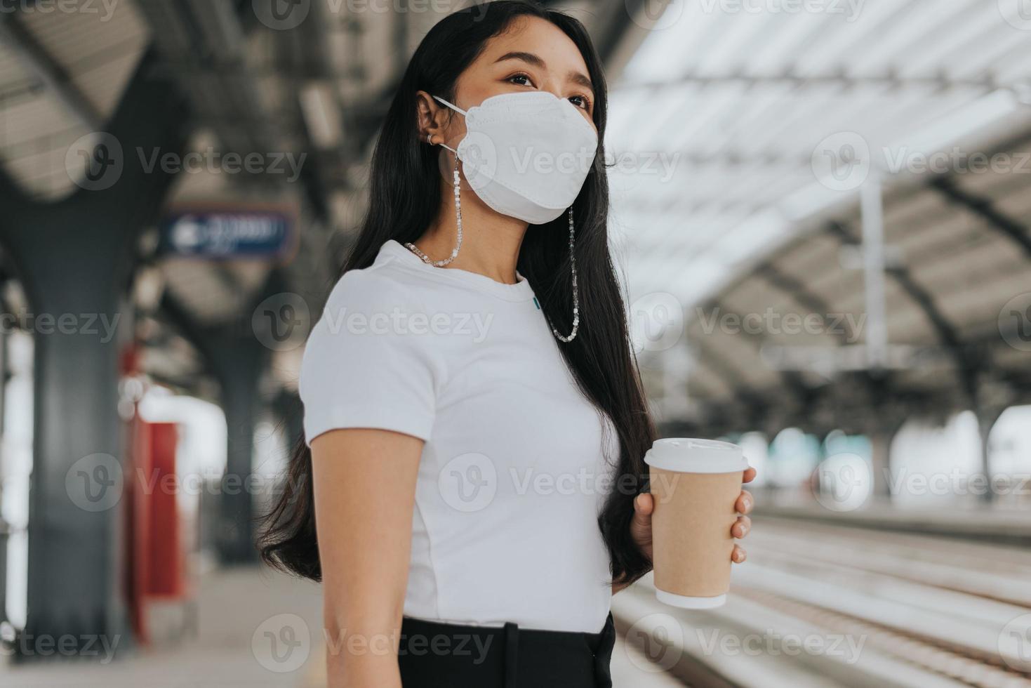 asiatisk kvinna som bär skyddsmask står och väntar på sky train. kvinna som bär kirurgisk skyddsmask i en kollektivtrafik. nytt normalkoncept. foto