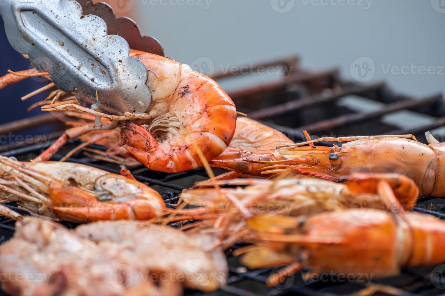 gosa upp stor räkor i en fräsande skaldjur grill på en fest. foto