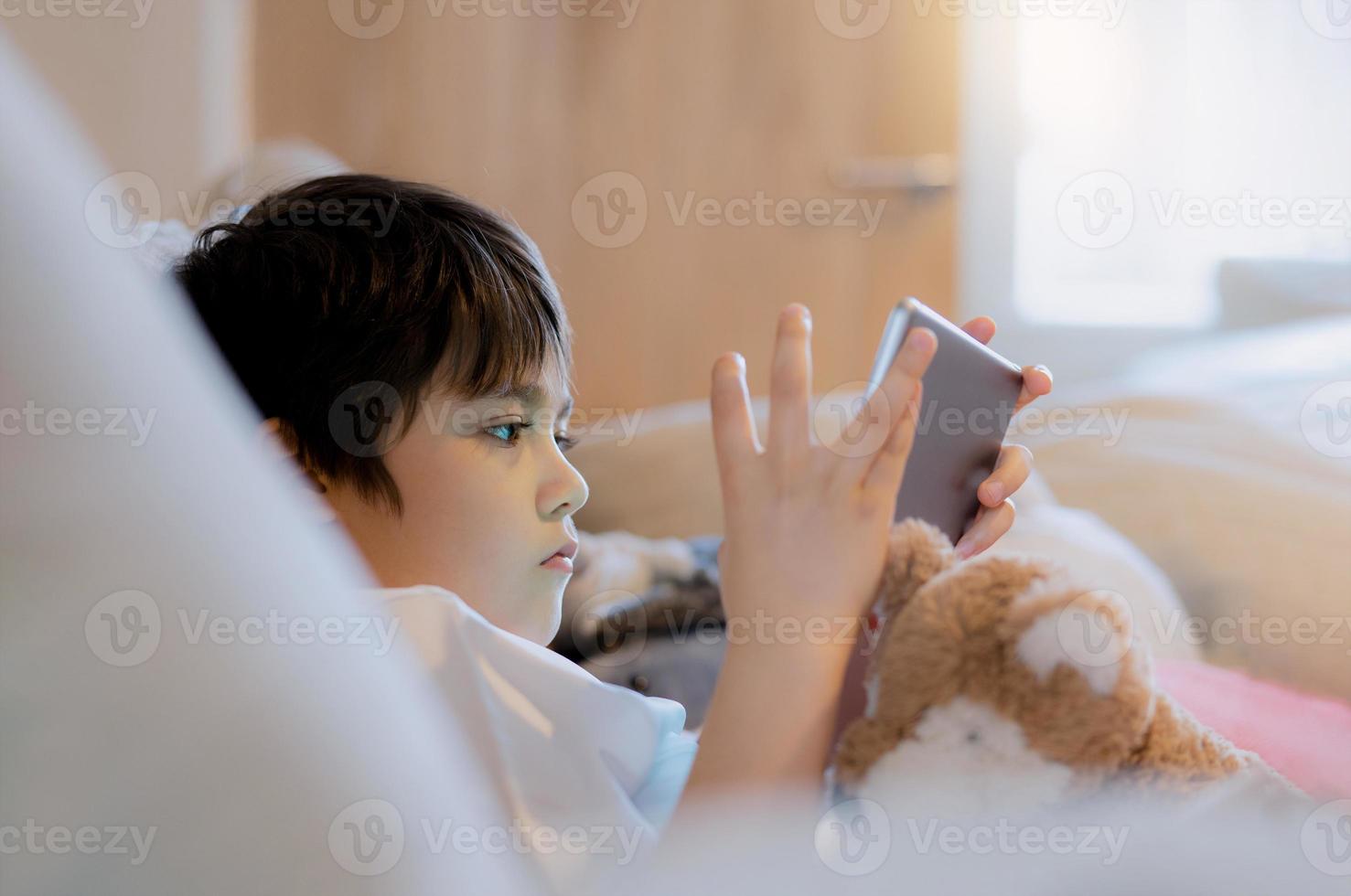 porträtt unge spelar spel på läsplatta Sammanträde på soffa, ung pojke läsning eller håller på med läxa uppkopplad på internet på hem, barn tittar på tecknad serie uppkopplad på digital pad.hem utbildning, tillbaka till skola begrepp foto