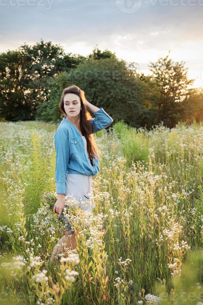 vacker flicka går på fältet på sommaren med vilda blommor. foto