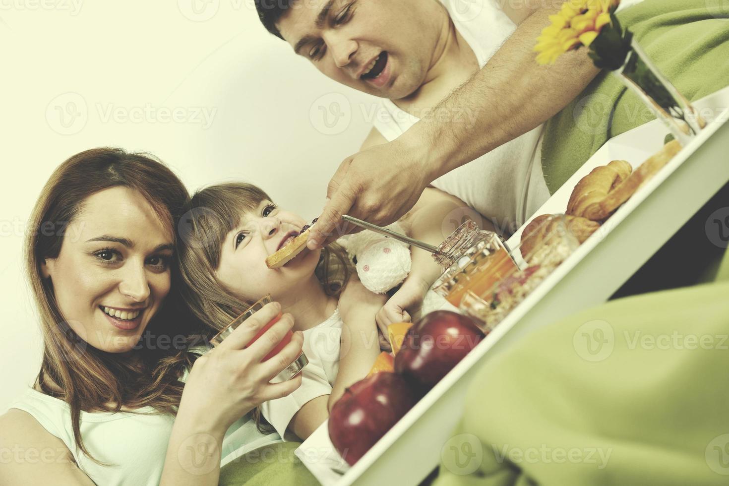 Lycklig ung familj äta frukost i säng foto