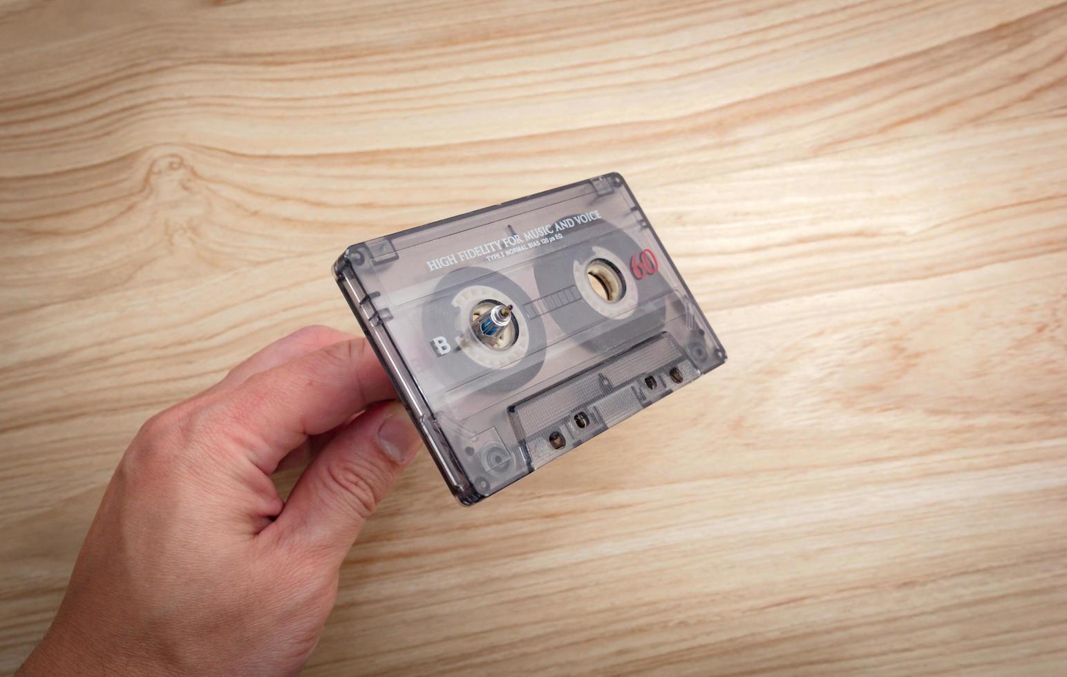 en vit mannens hand är spola tillbaka kassett band på en trä- bakgrund.. foto