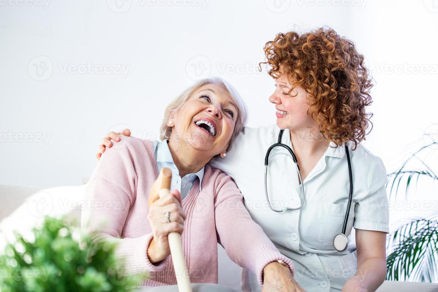 vänlig relation mellan leende vårdgivare i enhetlig och Lycklig äldre kvinna. stödjande ung sjuksköterska ser på senior kvinna. ung omtänksam härlig vårdgivare och Lycklig avdelning foto
