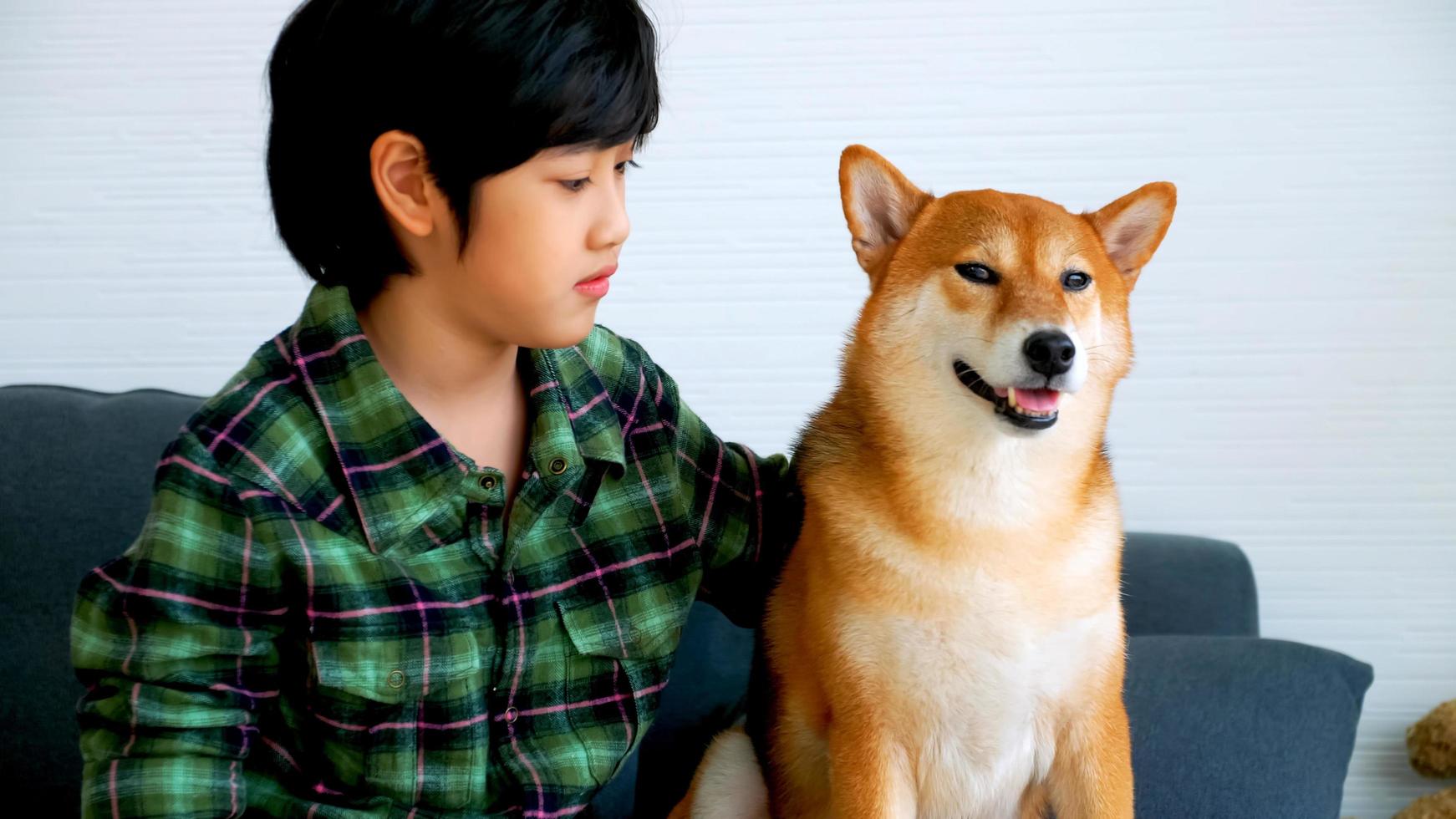 asiatisk pojke har roligt spelar med hans hund på soffa på Hem. foto