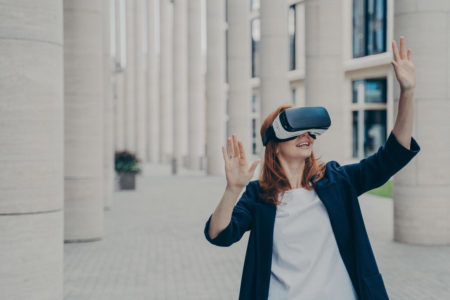 ung ingefära kvinna klädd formellt står utomhus och använder vr headset foto