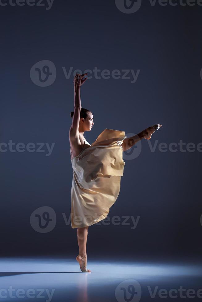ung vacker dansare i beige klänning dans på grå bakgrund foto