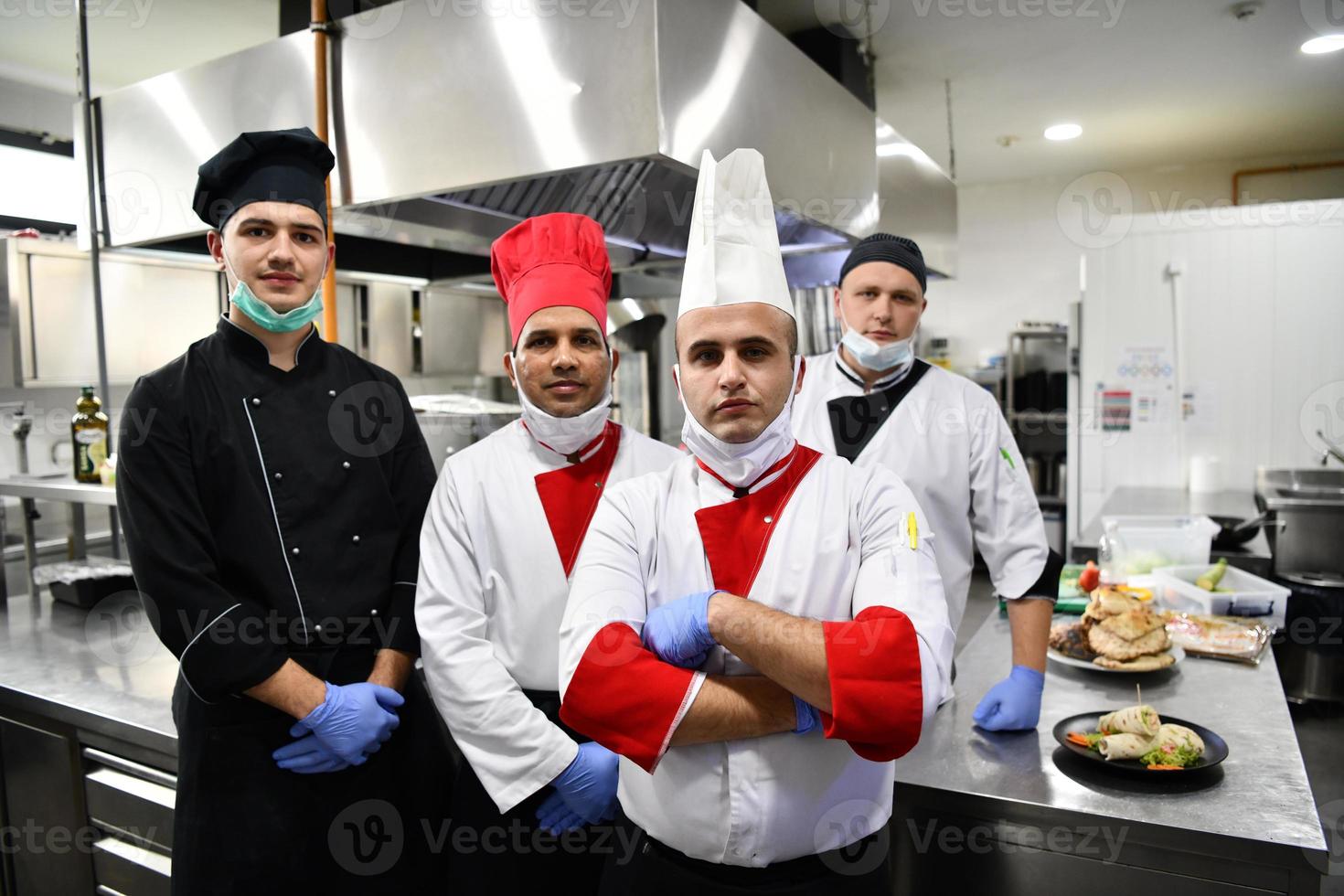 grupp kockar stående tillsammans i de kök på restaurang bär skyddande medicinsk mask och handskar i coronavirus ny vanligt begrepp foto