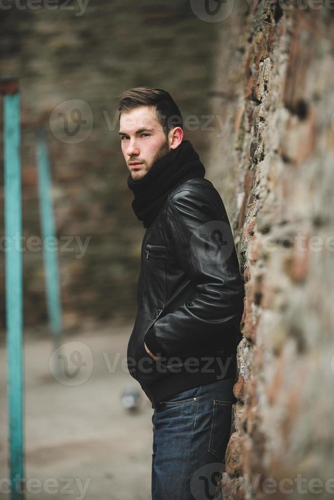 en man klädd i en svart jacka och jeans nära en sten vägg foto