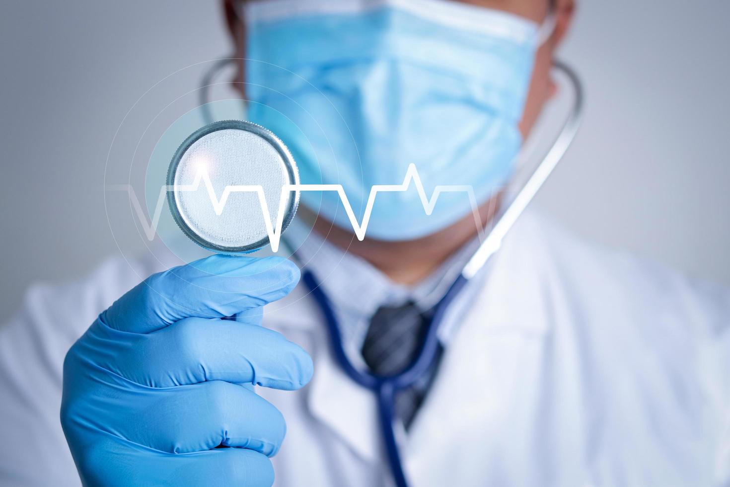 en läkare bär en blå mask innehar en stetoskop till undersöka de patient med en grafisk av de hjärta Vinka rytm. begrepp av sjukvård tjänster och medicinsk teknologi. upprätthålla kolla upp för coronavirus foto