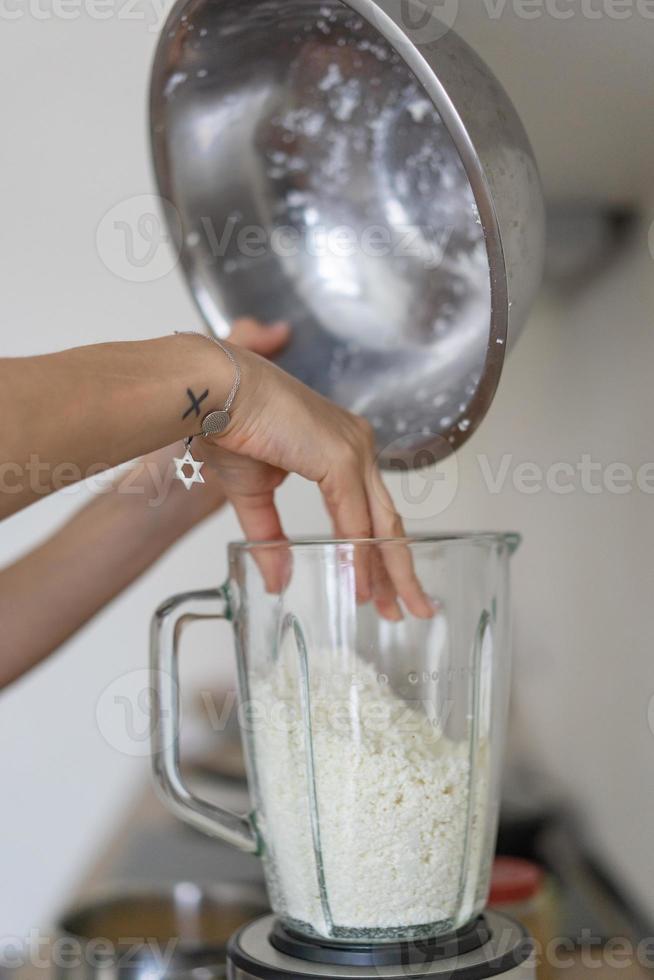 kvinna häller stuga ost in i en blandare i de kök foto