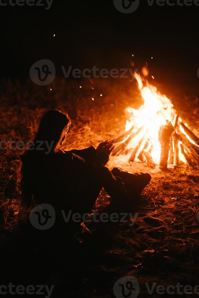 kvinna Sammanträde och få värma nära de bål i de natt skog. foto