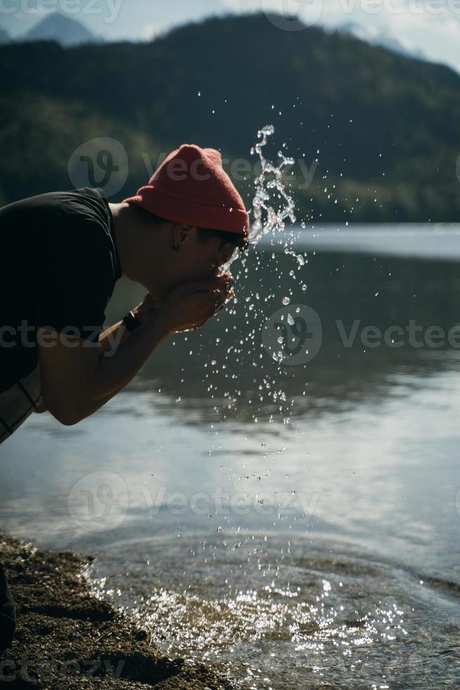 en man tvättar hans händer på de Strand av en skog sjö foto