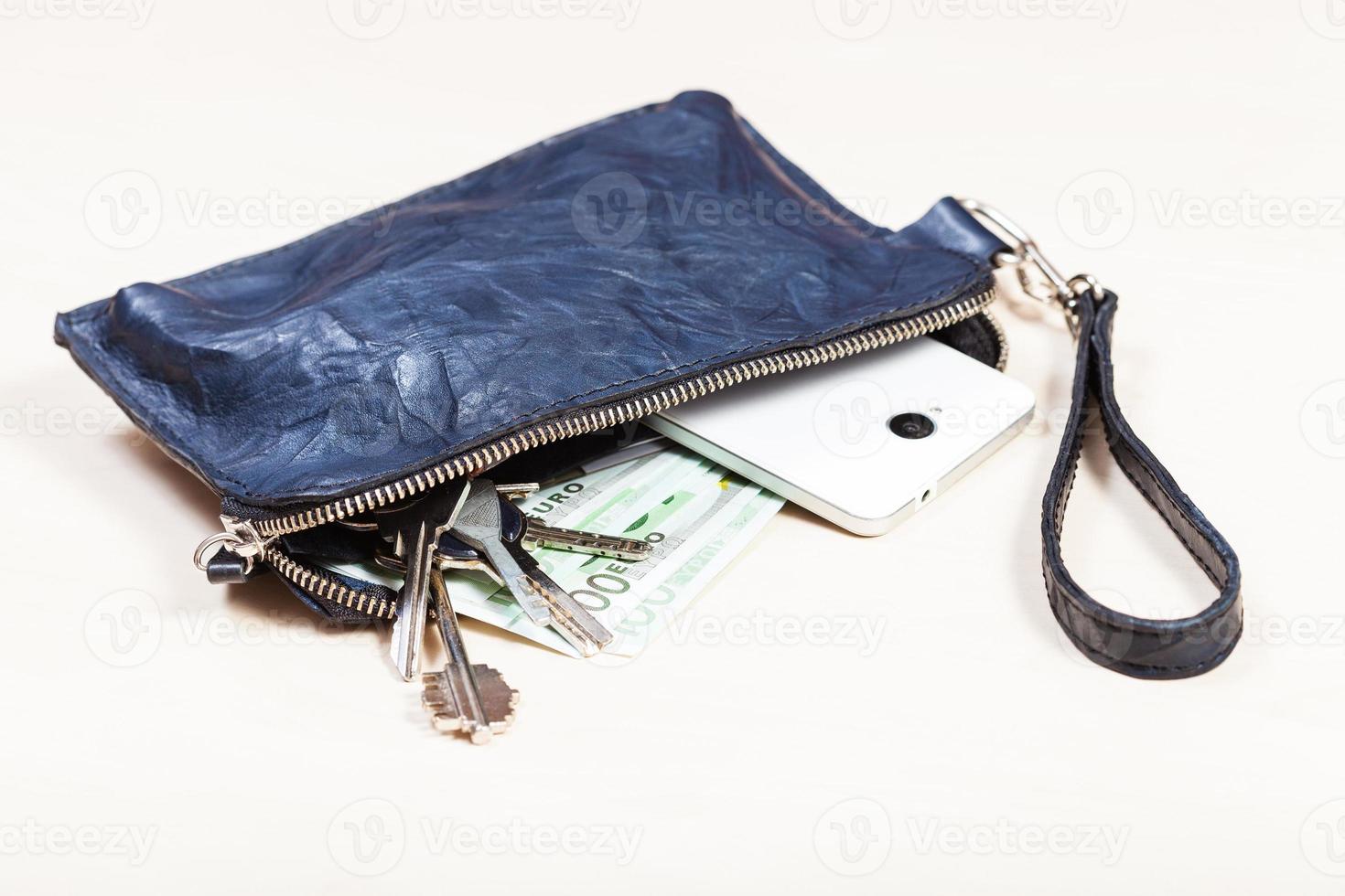 handväska med telefon, nycklar och euro anteckningar på tabell foto