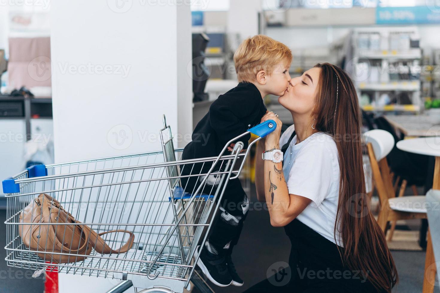 skön mor bär henne liten son i de mataffär vagn foto