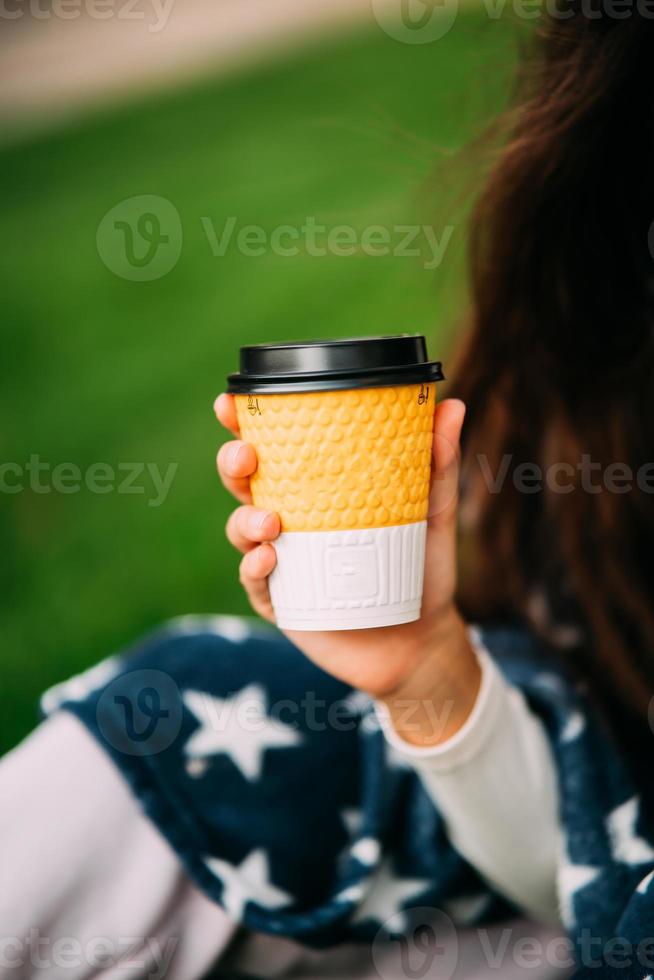 kvinnas hand innehav en papper glas av kaffe i de parkera foto