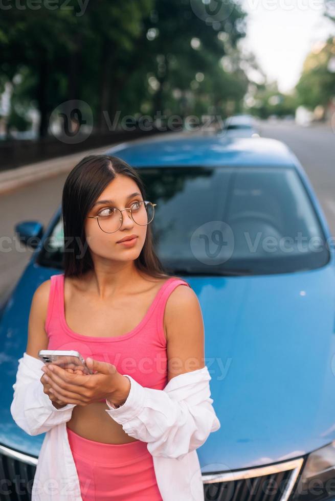 kvinna använder sig av mobil telefon nära bil på de gata foto