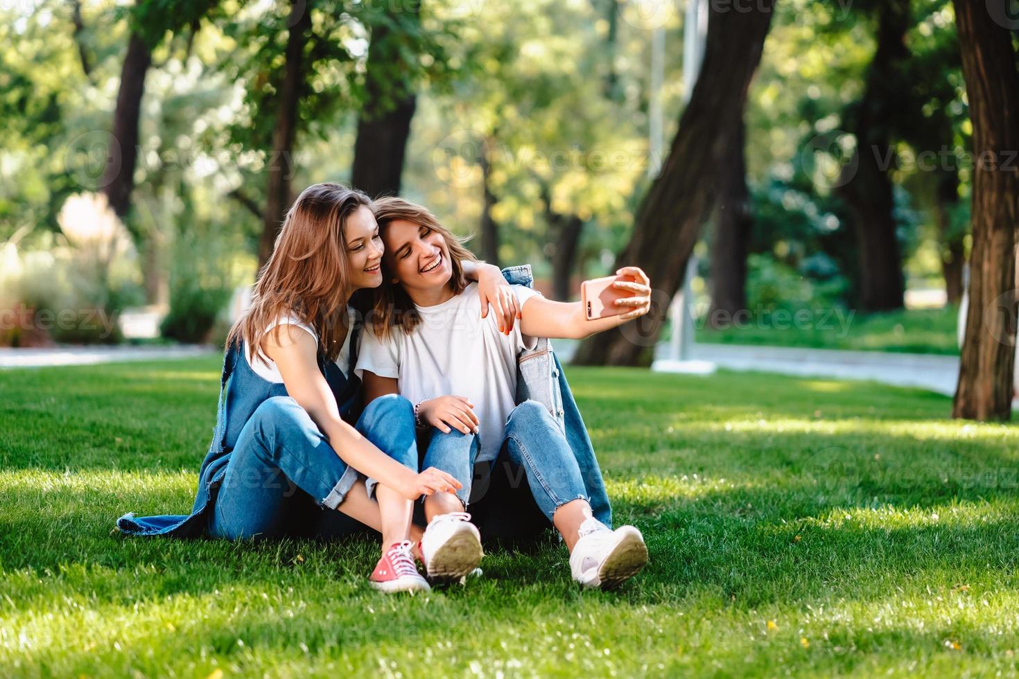 två kvinna vän Sammanträde i de parkera ha en resten ta en selfie foto