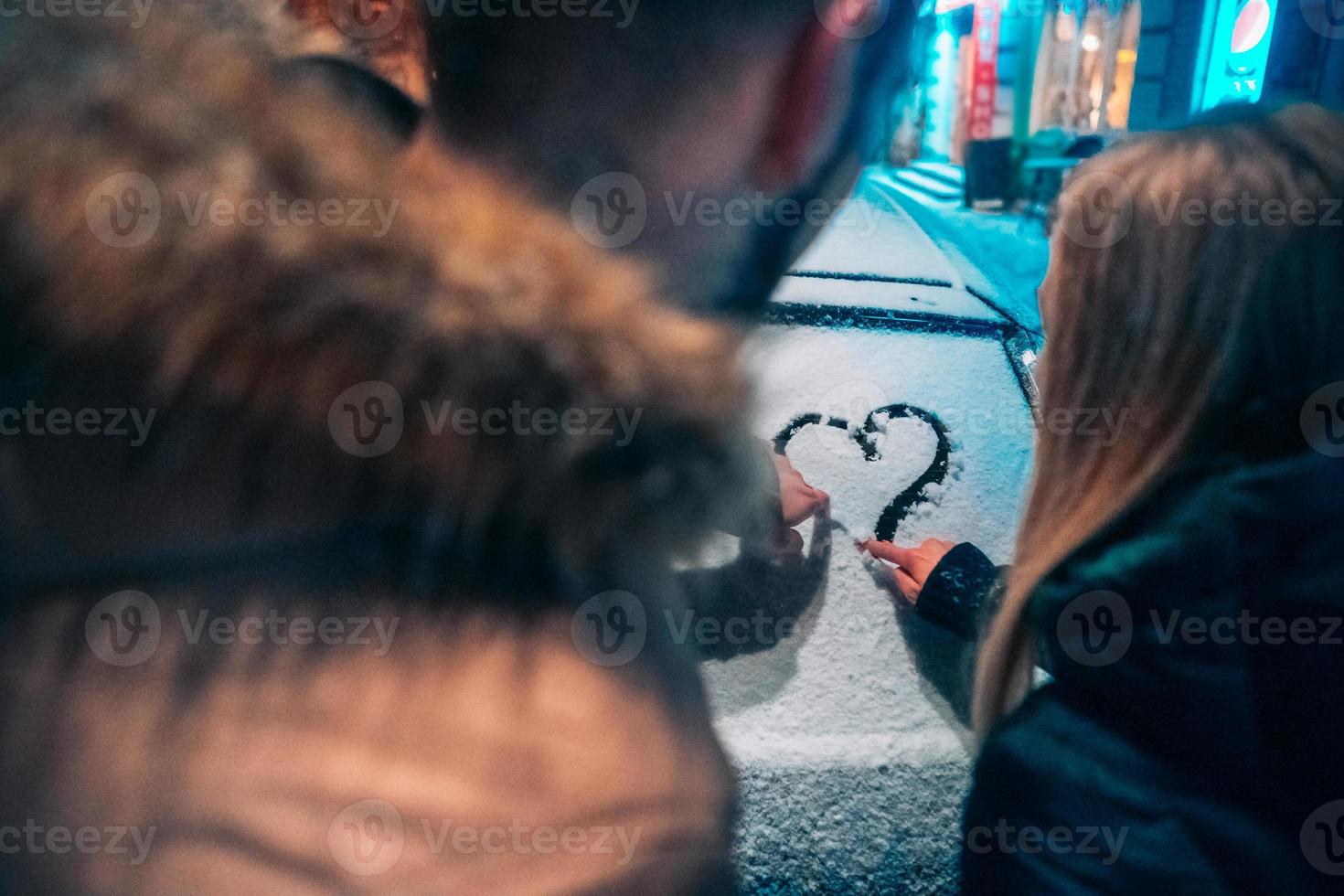 ung vuxen par drar en hjärta på snö täckt bil foto