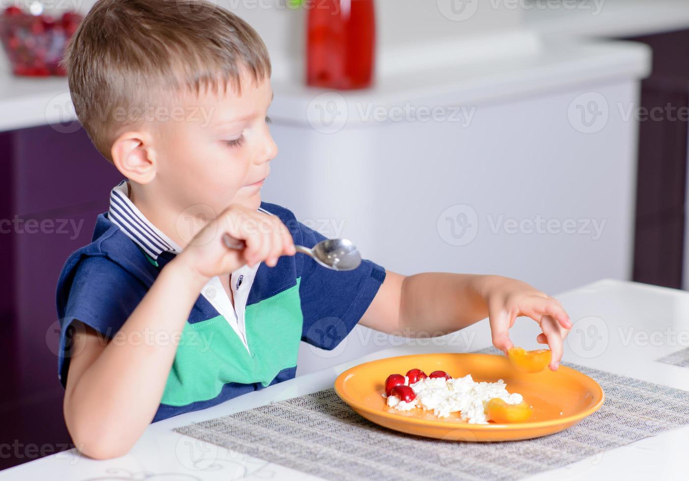 ung pojke äter tallrik med ost och frukt foto