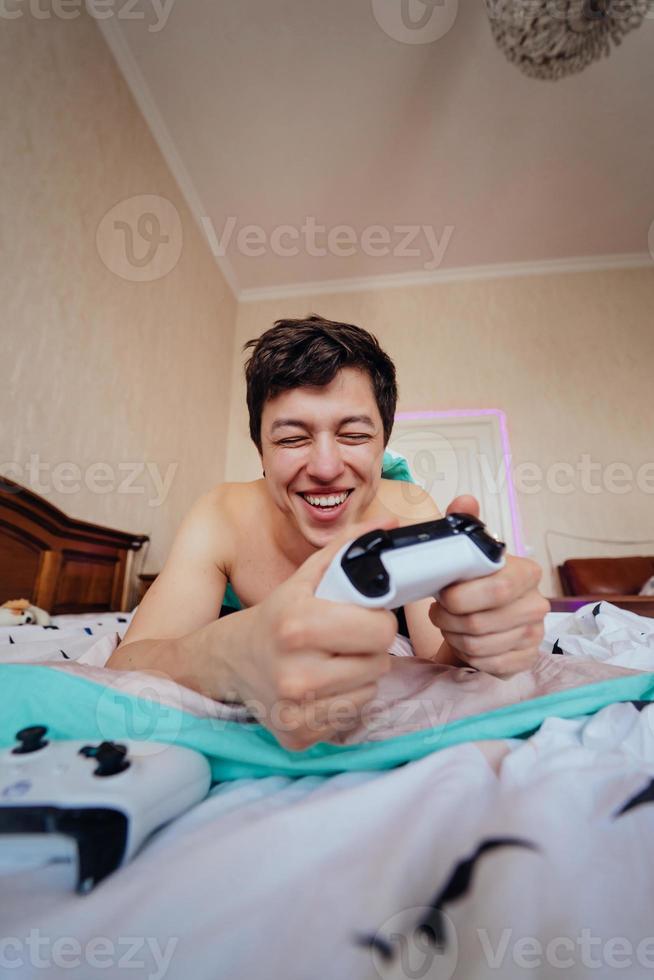 kille liggande i säng och spelar video spel, innehav kontrollant foto