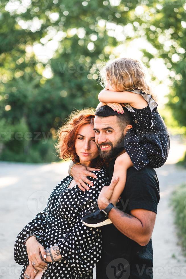 Lycklig föräldrar med en små dotter Sammanträde på de axlar foto