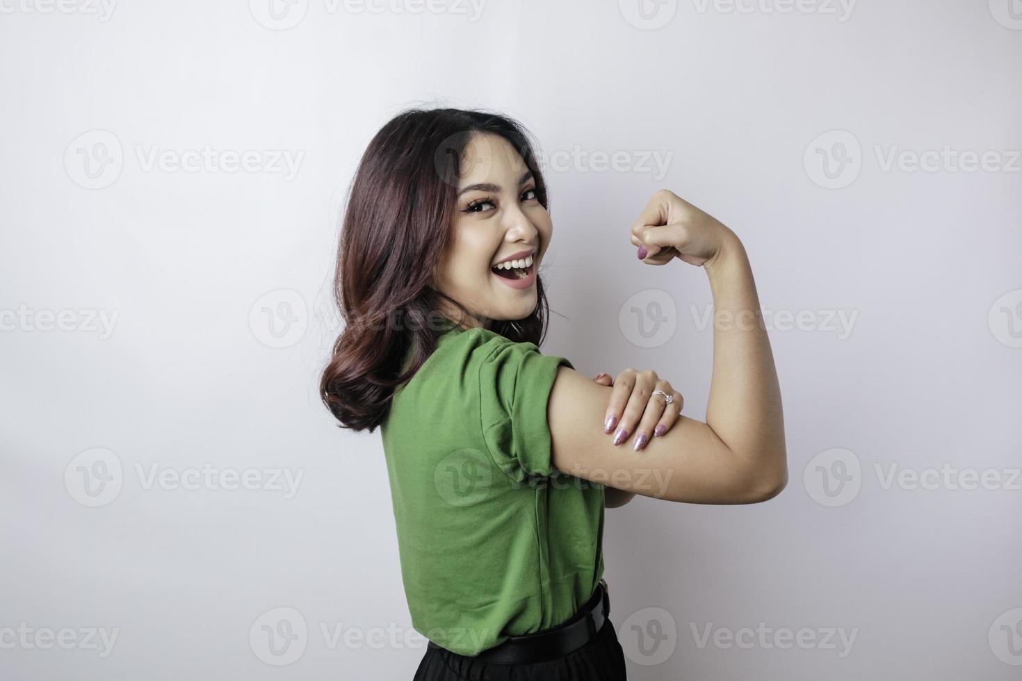 upphetsad asiatisk kvinna bär en grön t-shirt som visar stark gest förbi lyft henne vapen och muskler leende stolt foto
