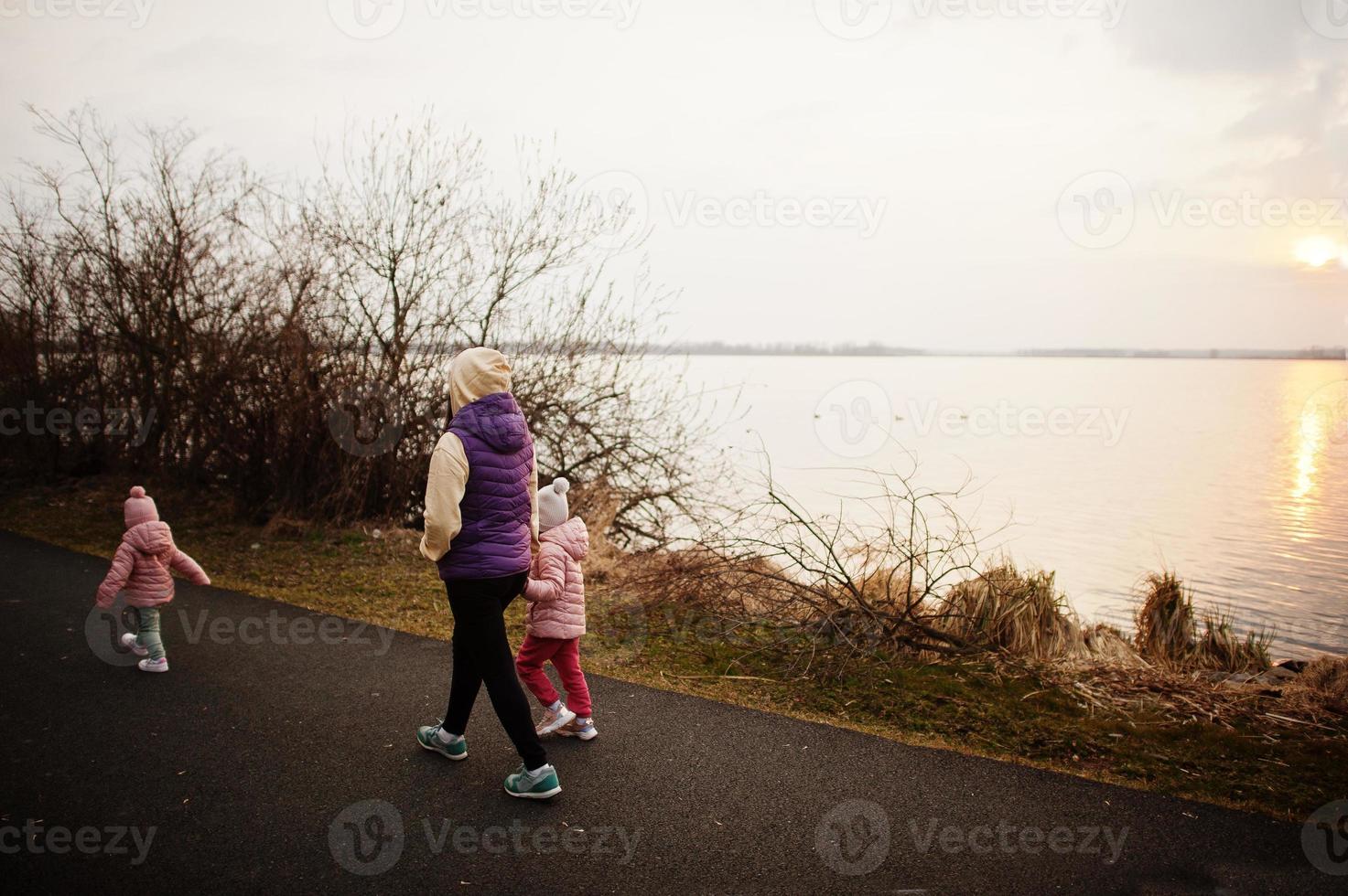 mamma med döttrar som går på stigen vid sjön. foto