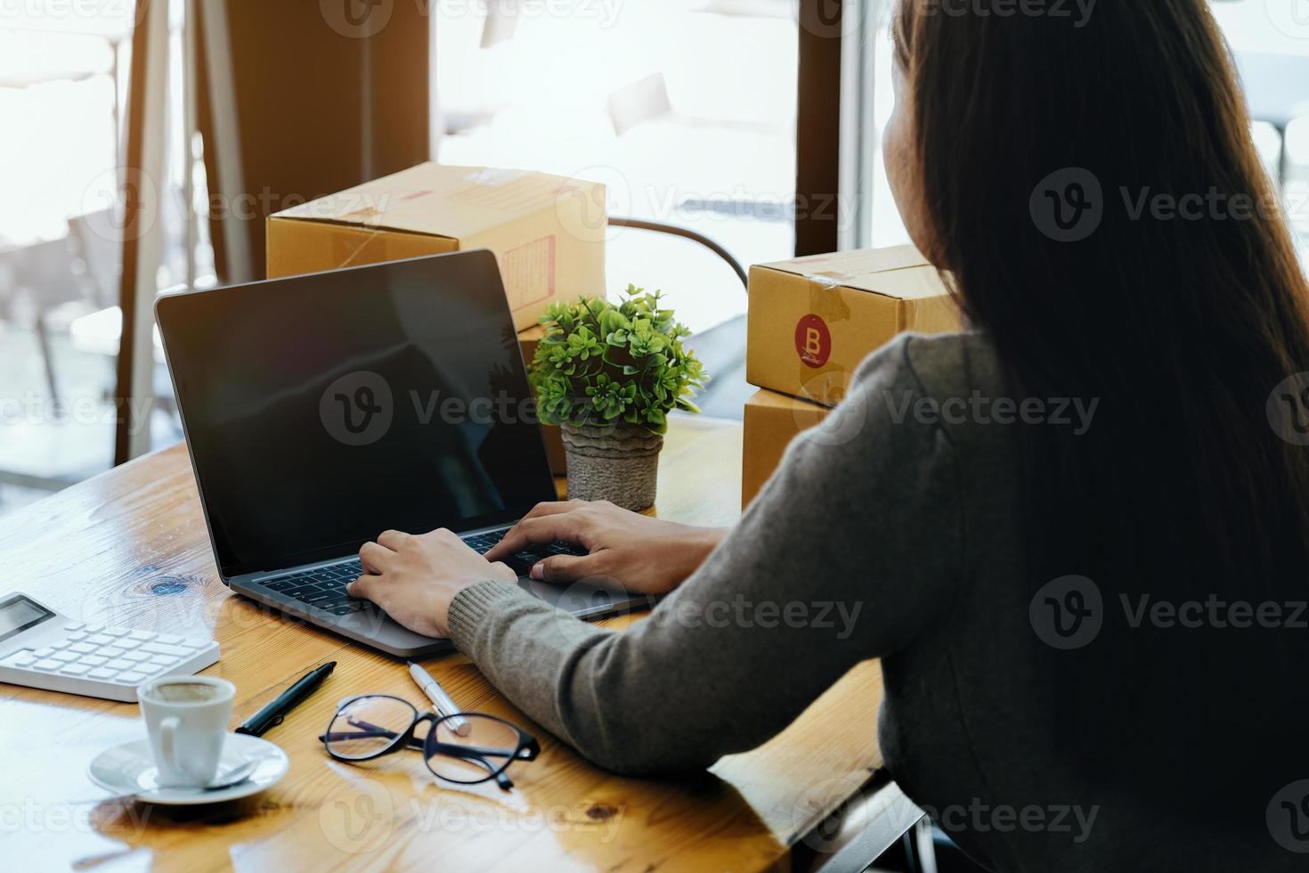 arbete från Hem. Lycklig kvinnor försäljning Produkter uppkopplad Start en små företag ägare förbi använder sig av bärbar dator dator till Beräkna priser och förbereda för porto. foto