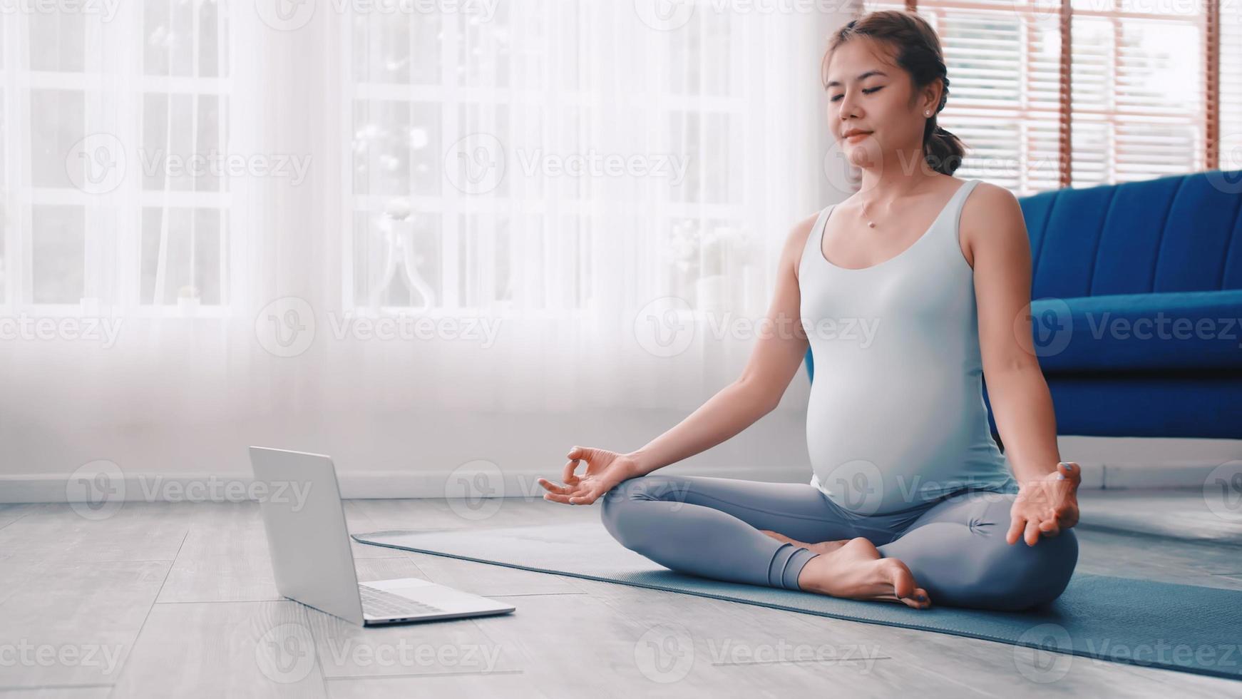 asiatisk gravid kvinna håller på med yoga övningar på Hem. foto