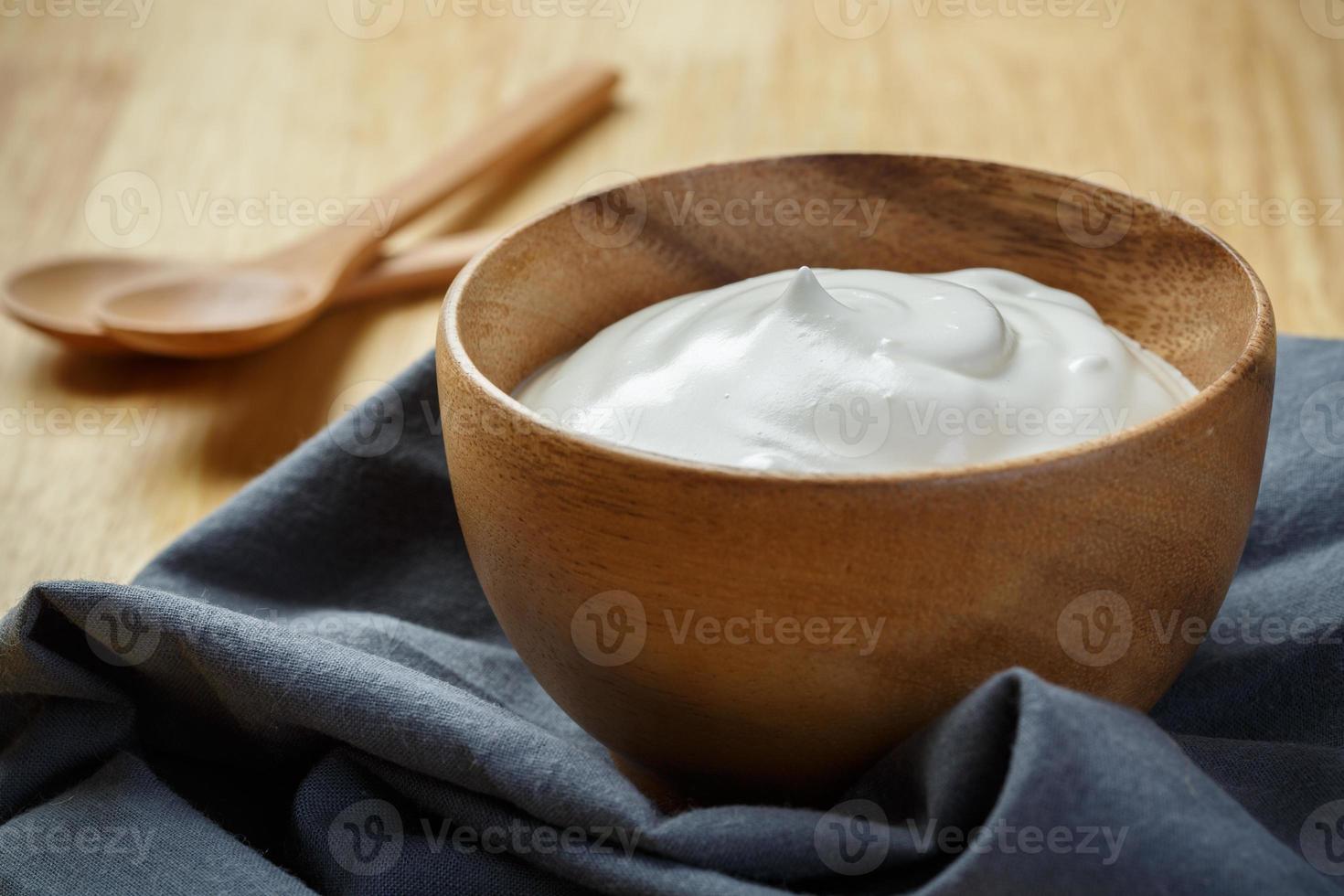 yoghurt i trä- skål på trä- bakgrund med blå bomull och trä- sked. enkel yoghurt. yoghurt. yoghurt. foto