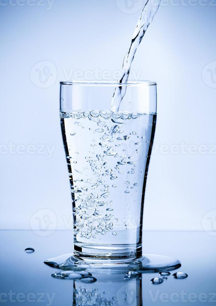 häller färsk ren vatten från flaska in i en glas på de tabell med vatten droppar, sjukvård och skönhet hydratisering begrepp foto