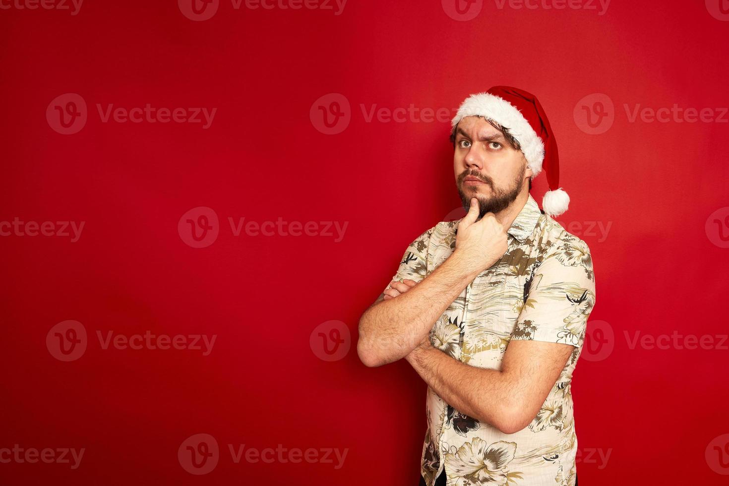 förbryllad förvirrad ung resande turist man i sommar tillfällig kläder jul santa hatt sätta hand på haka isolerat på röd studio bakgrund. passagerare reser på Semester. luft flyg resa begrepp foto