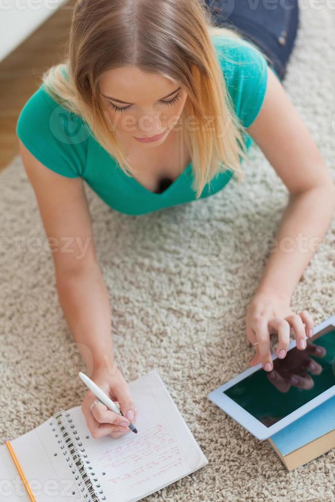 kvinna liggande på golvet gör sina läxor med hjälp av surfplatta foto