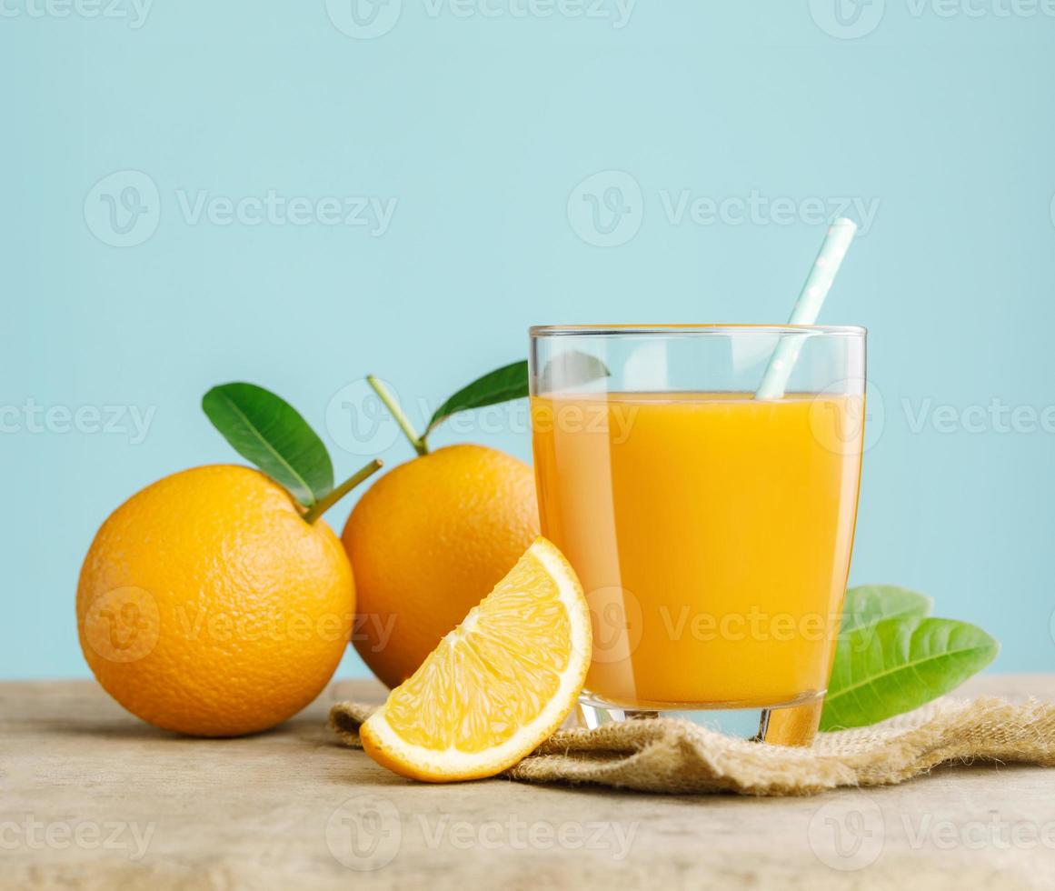 glas av färsk orange juice på trä- tabell, färsk frukt orange juice i glas med grupp av orange på blå bakgrund, selektiv fokus på glas foto