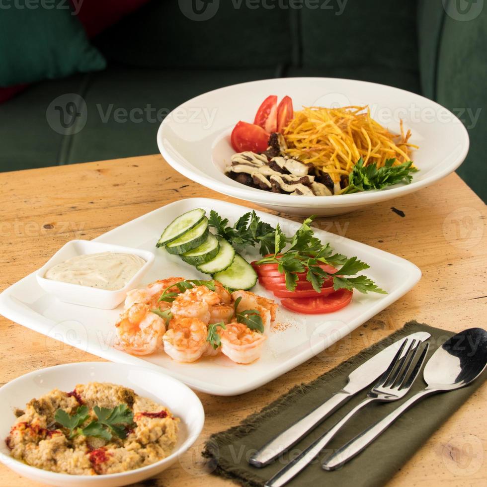ett middagsbord med måltider med hummus, räkor, grönsaker och nötkött foto
