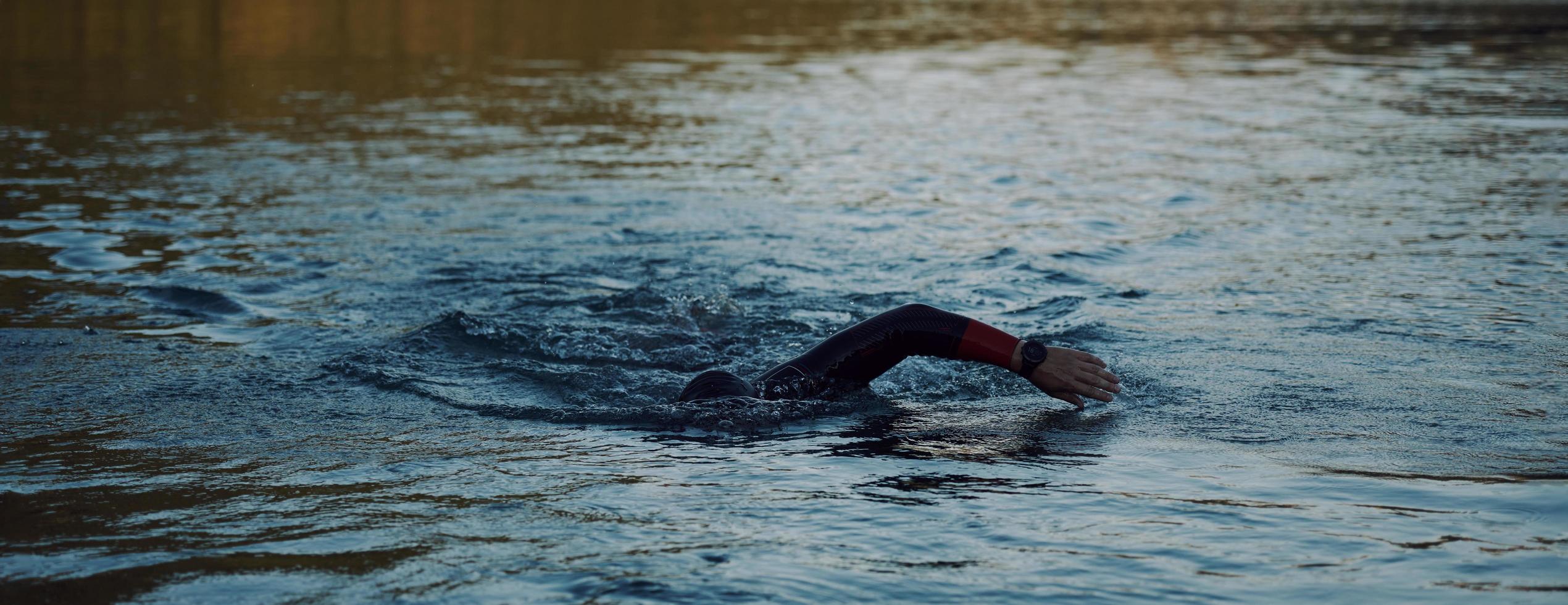 triathlon idrottare simmar på sjön i soluppgången bär våtdräkt foto