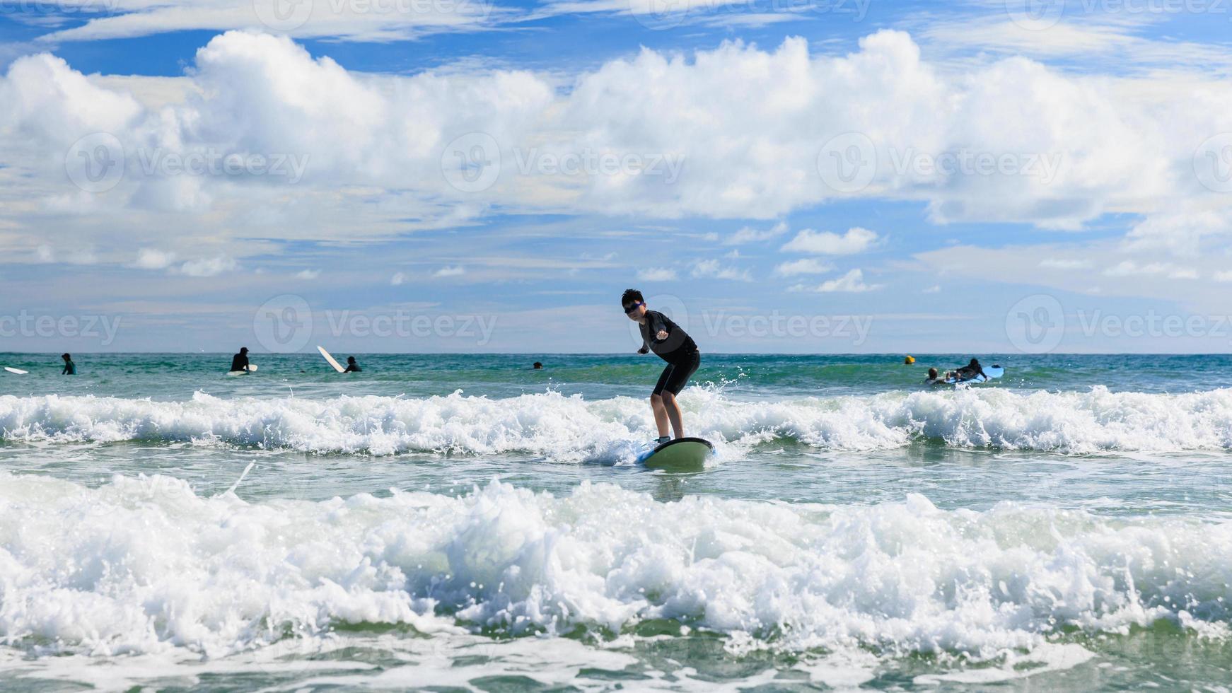 ung pojke först Framgång och står på en mjuk styrelse medan praktiserande surfing i en nybörjare klass. tonåring aktivt balansering på vatten sporter Utrustning och påfrestande ny upplevelser. foto