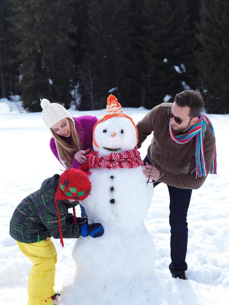 lycklig familj som gör snögubbe foto