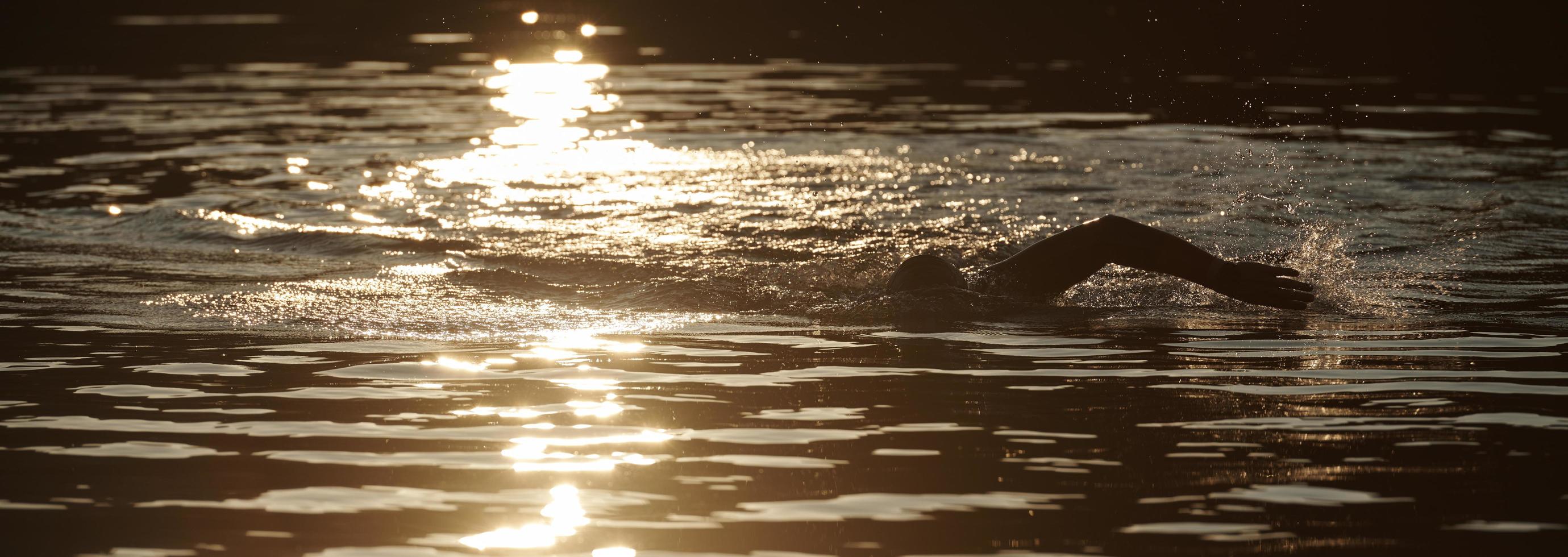 triathlon idrottare simmar på sjön i soluppgången bär våtdräkt foto